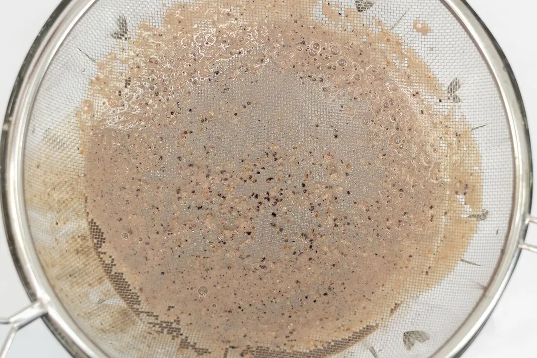 A batch of protein shake prepared by the Cuisinart blender is checked for smoothness by being drained through a stainless steel mesh strainer.