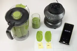 The NutriBullet motor base and its container stand on a table, accompanied by a glass filled with a green smoothie. Next to it, a white paper features two distinct smoothies spread while a smartphone showcases the blending time of 59 seconds.