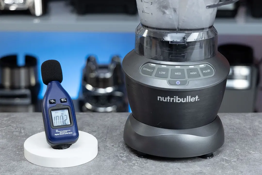 The NutriBullet ZNBF30500Z blender is on a table, accompanied by a sound level meter displaying its noise level nearby. In the background, other blenders that we tested sit on a nearby shelf.