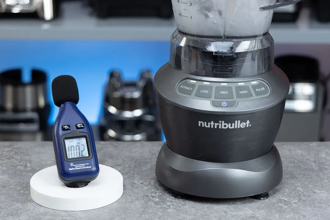 The NutriBullet ZNBF30500Z blender is on a table, accompanied by a sound level meter displaying its noise level nearby. In the background, other blenders that we tested sit on a nearby shelf.