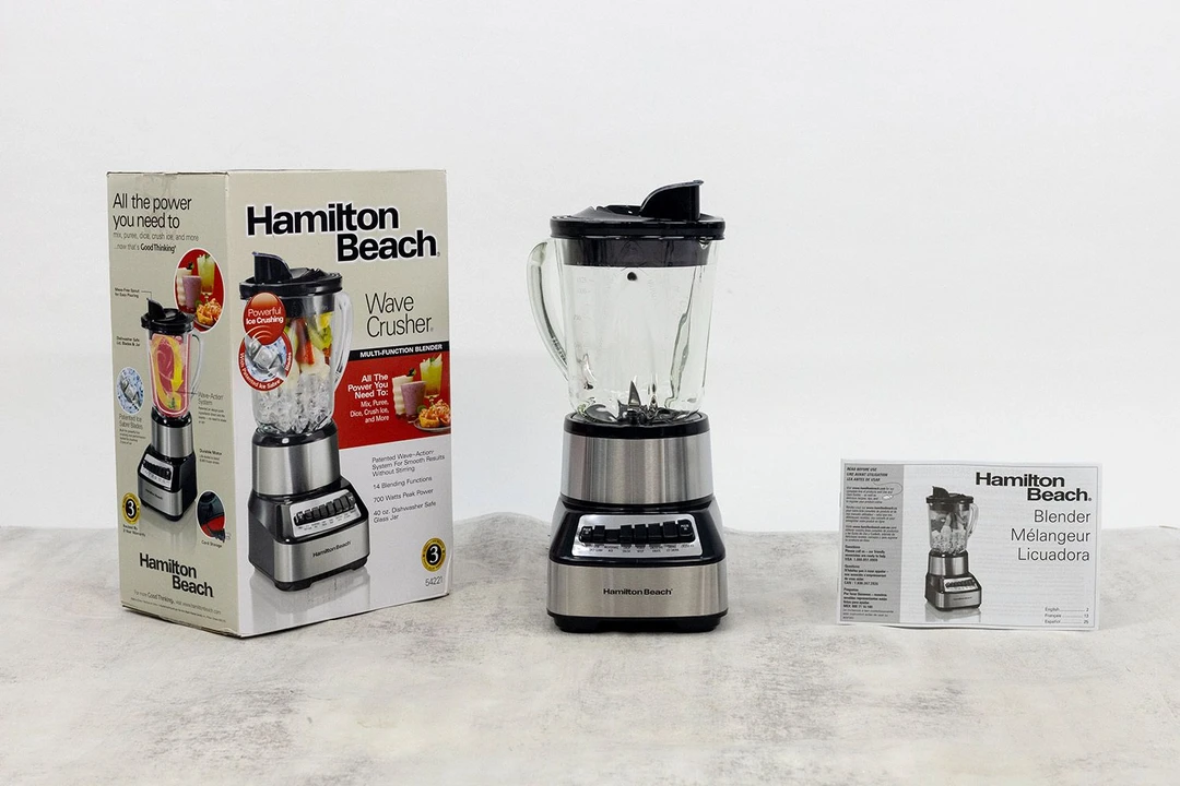 The Hamilton Beach blender stands on a table, with a user manual and a carton box by its sides.