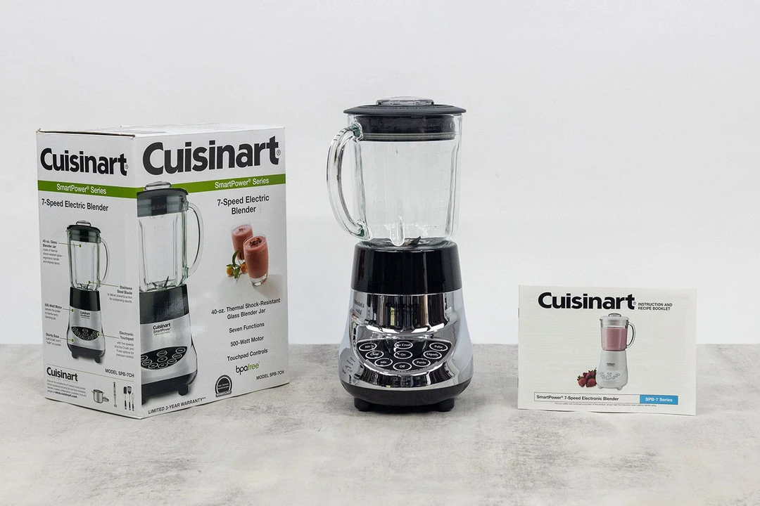 The Cuisinart blender stands on a table, with a user manual and a carton box by its sides.