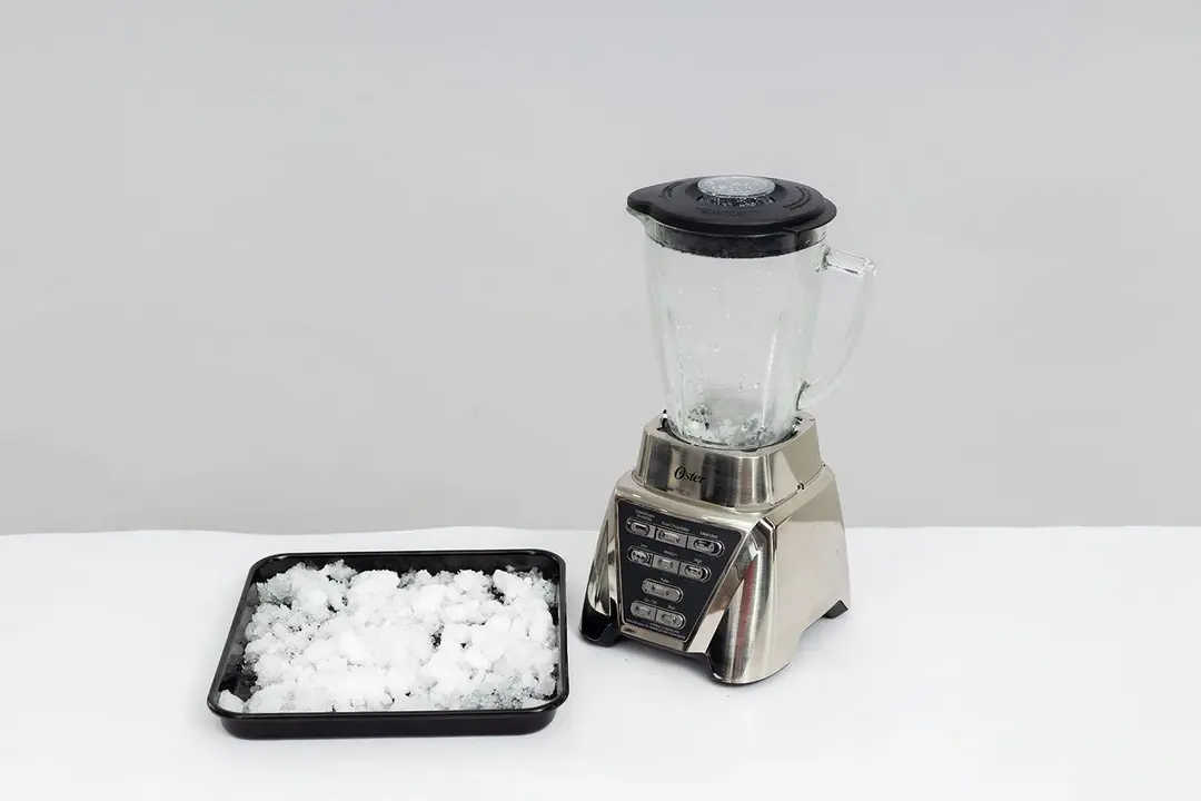 The Oster Pro blender is beside a black tray containing its crushed ice.