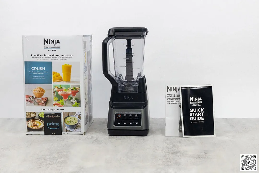 The Ninja BN701 blender stands on a table, with a user manual and a carton box by its sides. 