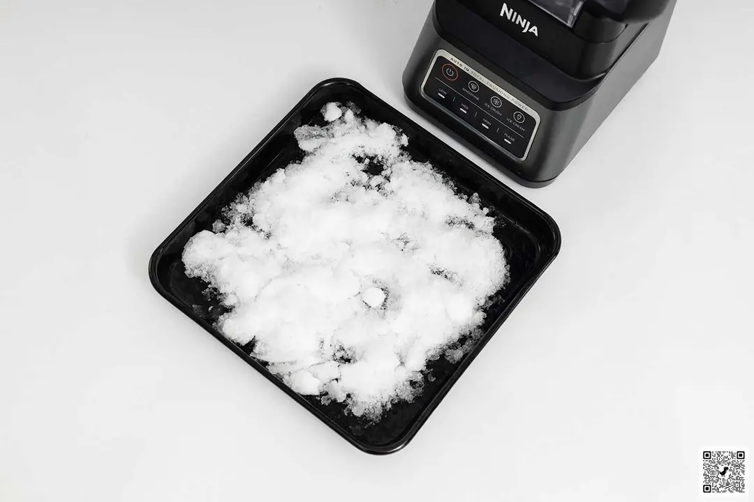 The Ninja BN701 Professional Plus blender is beside a black tray containing its crushed ice.