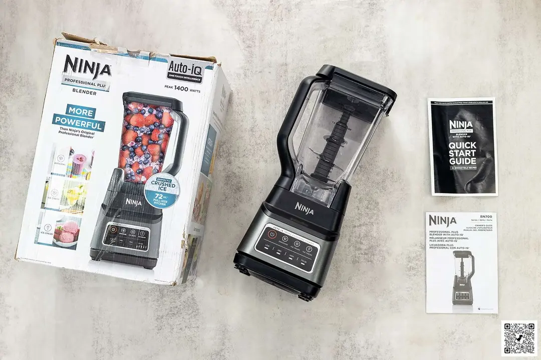 A display of the  Ninja BN701 Professional Plus blender blender and its accessories, including the user manual and a carton box, on a table.