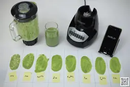 The Black+Decker Crush Master blender motor base and its container stand on a table, accompanied by a glass filled with a green smoothie. Next to it, a white paper features three distinct smoothie samples while a smartphone showcases the blending time of 4 minutes.