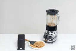 The Cuisinart SPB-7CH SmartPower is beside a white plate containing almond butter with a spatula and a smartphone revealing a blending time of 4 minutes.