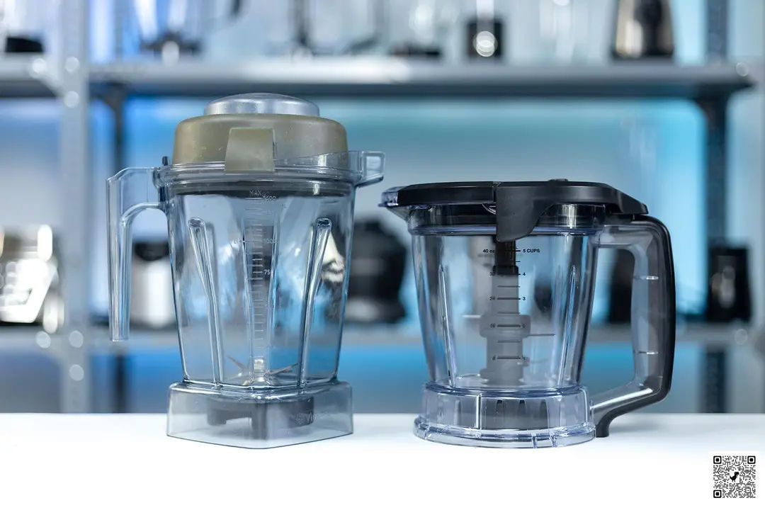 The blending containers of the Vitamix E310 and Ninja AMZ.. blender are displayed side by side. In the backdrop, various models of blenders occupy the shelves.