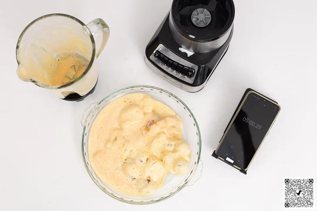 The Hamilton Beach Wave Crusher motor base stands beside a glass bowl which contains a portion of the smoothie it produced. Next to it, a smartphone displays a blending time of 5 minutes. 