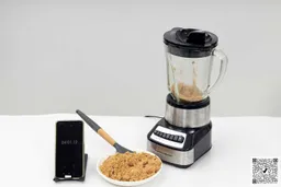 The Hamilton Beach Wave Crusher is beside a white plate containing almond with a spatula and a smartphone revealing a blending time of 4 minutes.