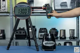 the Black+Decker blender motor base on table, hand pressing digital tachometer attached to tripod, different blenders in background. 