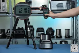 The Hamilton Beach Wave Crusher blender motor base on table, hand pressing digital tachometer attached to tripod, different blenders in background.