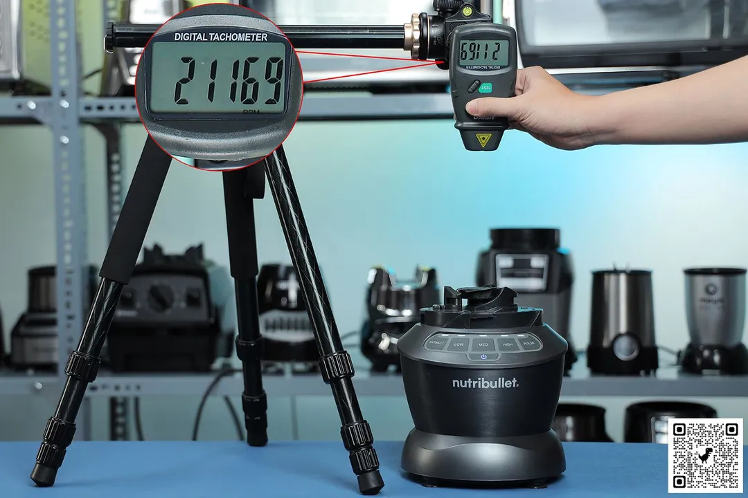 The NutriBullet ZNBF30500Z motor base on a table with a hand pressing a digital tachometer on a tripod. Different blenders are visible in the background.
