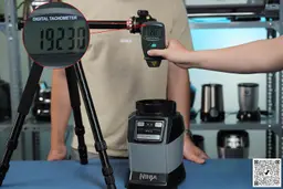 The Ninja AMZ493BRN motor base on a table with a hand pressing a digital tachometer on a tripod. Different blenders are in the background.