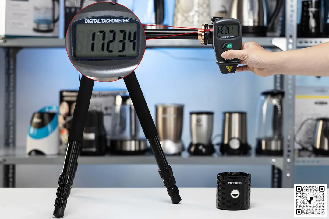 The Popbabies motor base on table with a hand pressing a digital tachometer on a tripod. Different blenders are visible in the background.