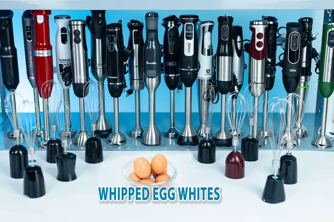 Nineteen immersion blenders lying on a table with ingredients and necessary tools for the whipped egg-white test, including eggs contained in a bowl, next to them. 