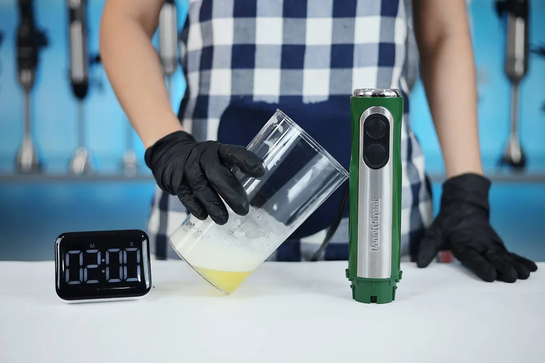 Someone is tilting the plastic beaker at an angle of 45 degree which contains the failed beaten egg-white of the Peach Street hand blender after the total whipping time of 2 minutes.