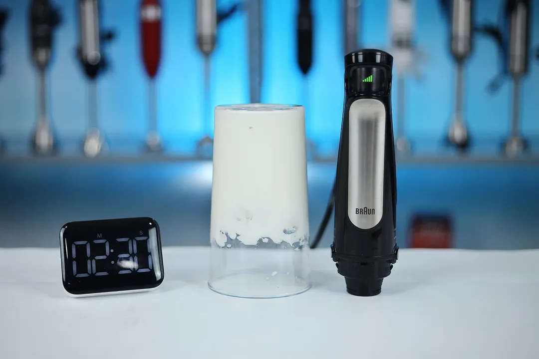 The Braun MQ7035X immersion blender stands next to a glass of whipped egg whites forming stiff peaks, with a digital timer showing "2:30" in the foreground.