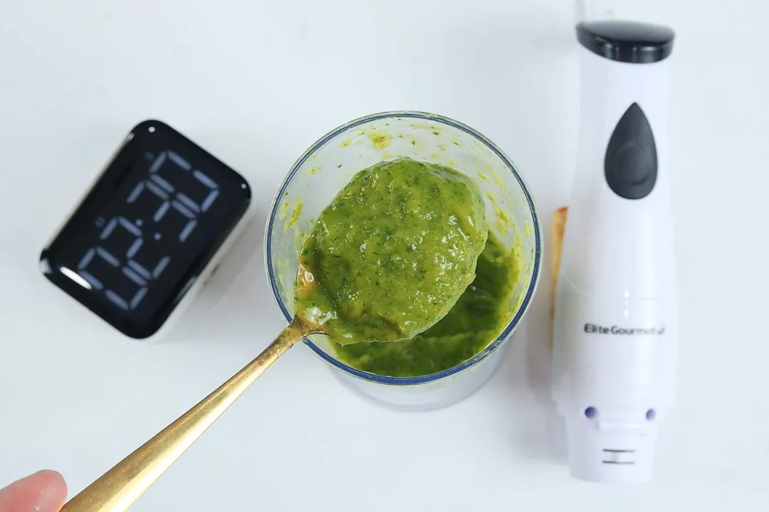Scooping a spoon of smoothie from the plastic beaker to check its texture after the Elite Gourmet EHB-2425X Hand Blender had completed the test in 2:30 seconds.