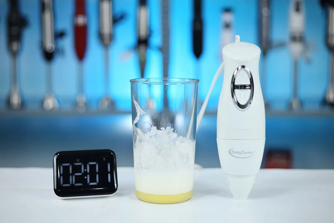 A digital timer shows 2:01 on a kitchen counter, with a beaker containing unsuccessfully beaten egg whites next to the Betty Crocker immersion blender. 
