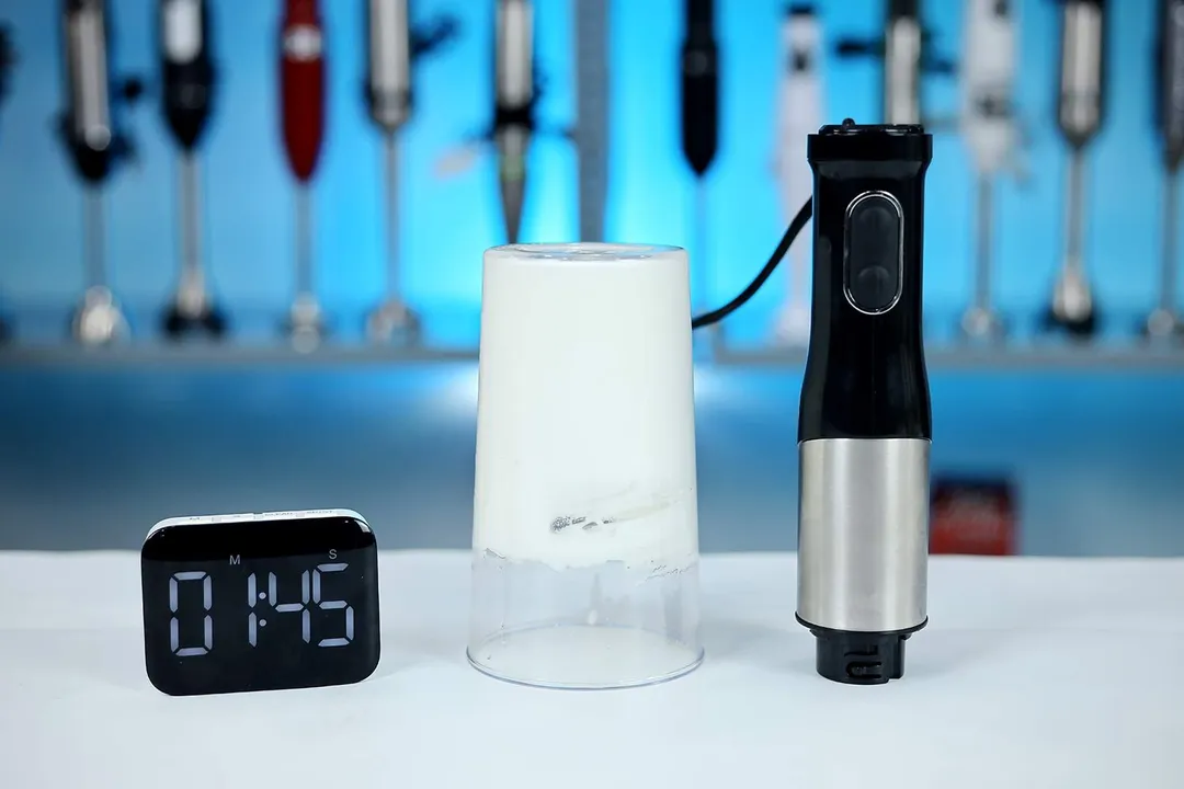 The plastic beaker containing beaten egg-white of the LINKchef immersion blender is put upside down on the table;  a smartphone displaying 1 minute and 45 seconds by its sides.