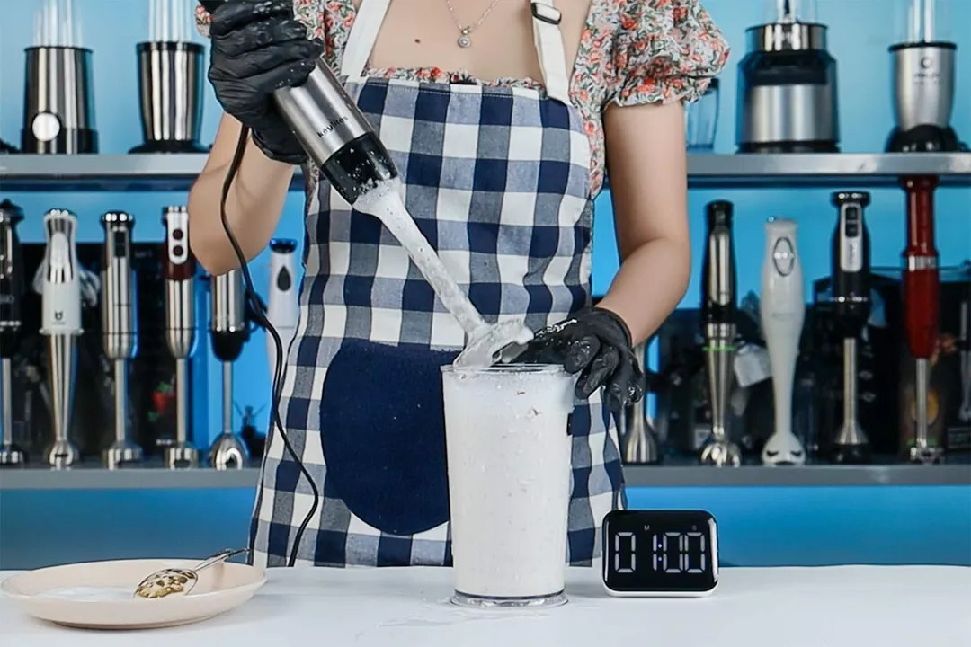 Person making almond milk using an immersion blender, timer clock next to it
