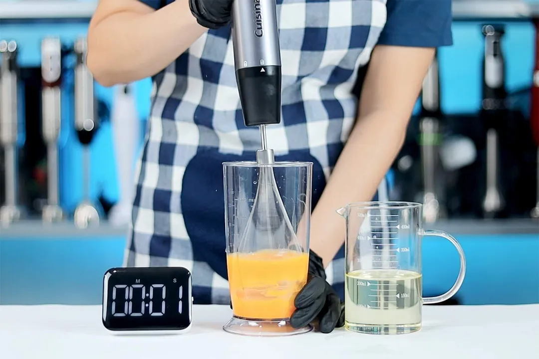 person beating egg yolk and oil using immersion blender, timed with clock