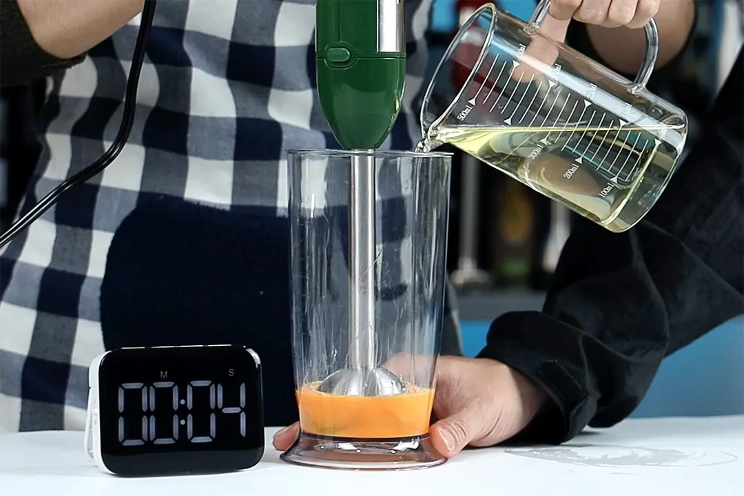 Oil being poured into blender beaker containing egg yolk