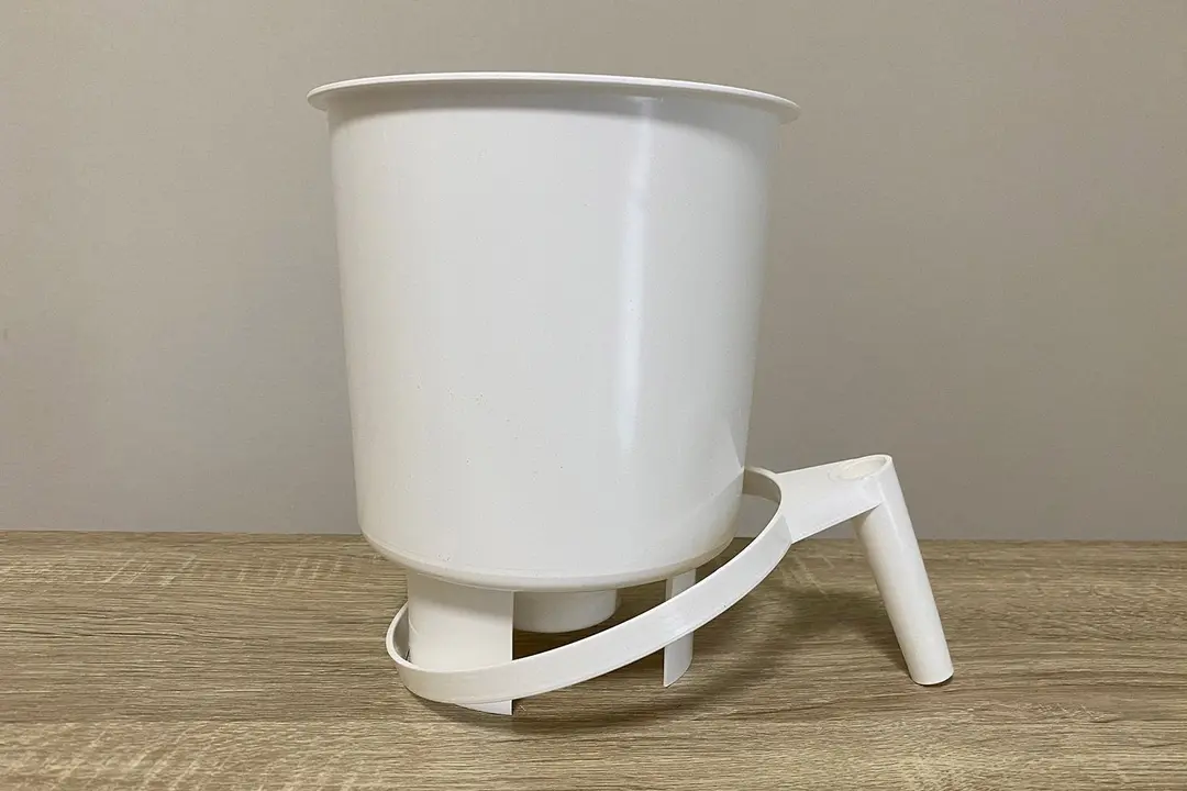 The white plastic brew vessel of the Toddy Cold Brew System on a wooden counter with the handle resting on the ground.