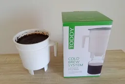 The Toddy Cold System brew vessel filled with coffee grounds and water pictured next to its packaging box.