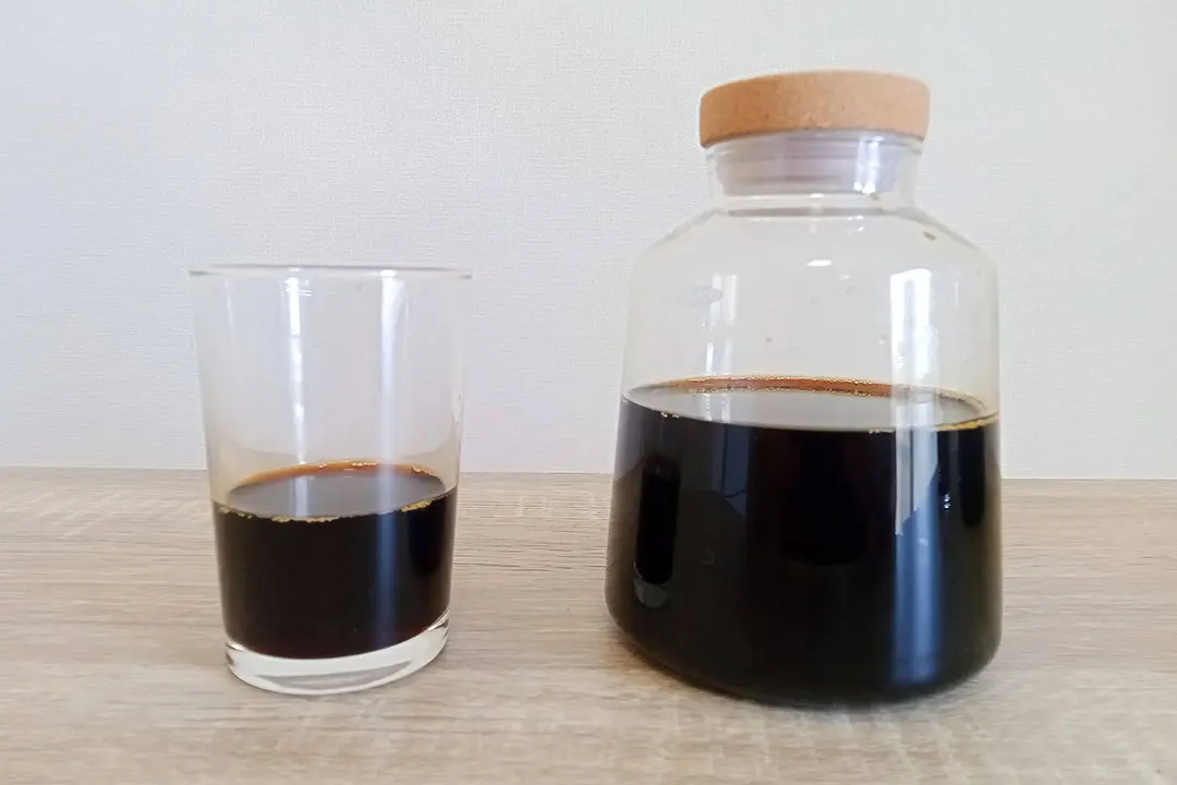 The Oxo Compact cold brew carafe filled with coffee standing next to glass a third filled with coffee.