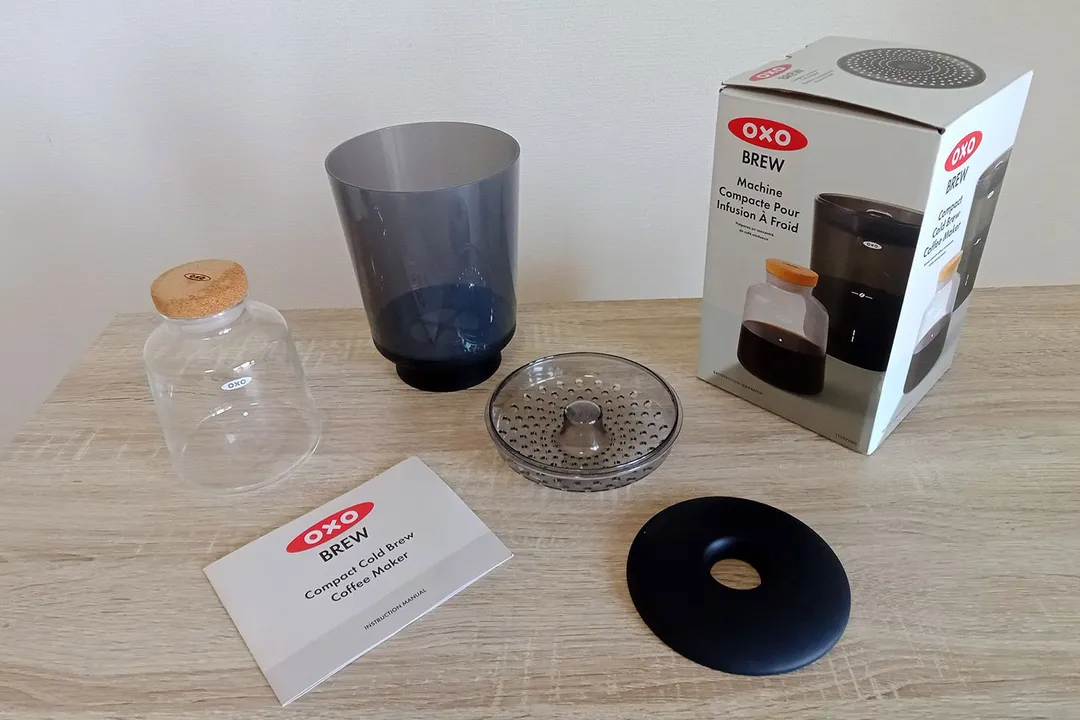 The unboxed Oxo compact cold brew coffee maker. Pictured next to the box is the brew vessel, the carafe, and user manual.