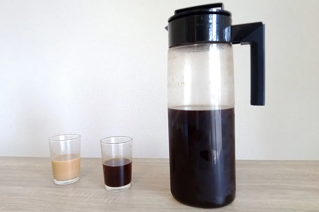 The Takeya cold brew coffee maker with a freshly made brew and two cups to the left: one straight coffee, the other with milk.