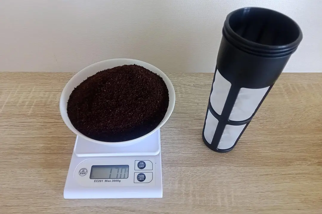 The immersion filter of a cold brew coffee maker with a bowl of coffee grounds to the left resting on a scale.