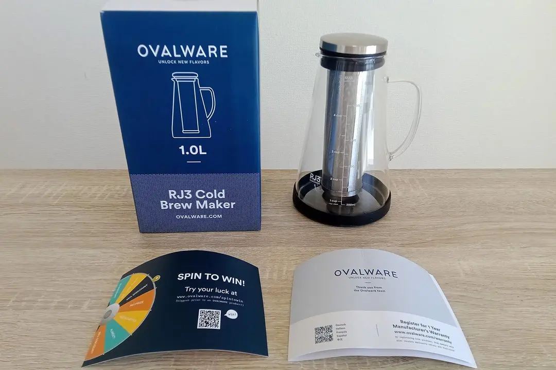 The unboxed contents of the Ovalware RJ3 cold brew coffee maker: the box, the glass carafe with the filter, and user manual.