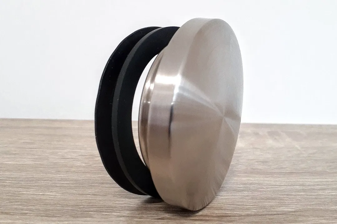 The stainless steel stopper with a rubber silicone ring resting on its side on a wooden countertop.