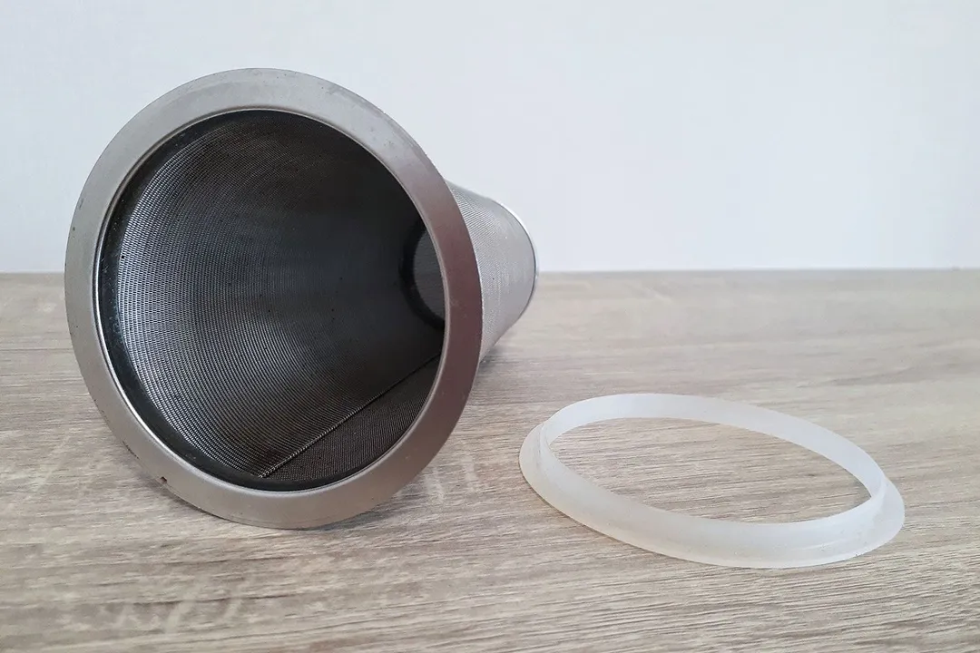 The stainless steel filter of a cold brew coffee maker and a silicone seal to the right resting on a wood countertop.