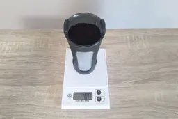 The filter of a cold brew coffee maker filled with grounds and standing on a scale showing 100g.
