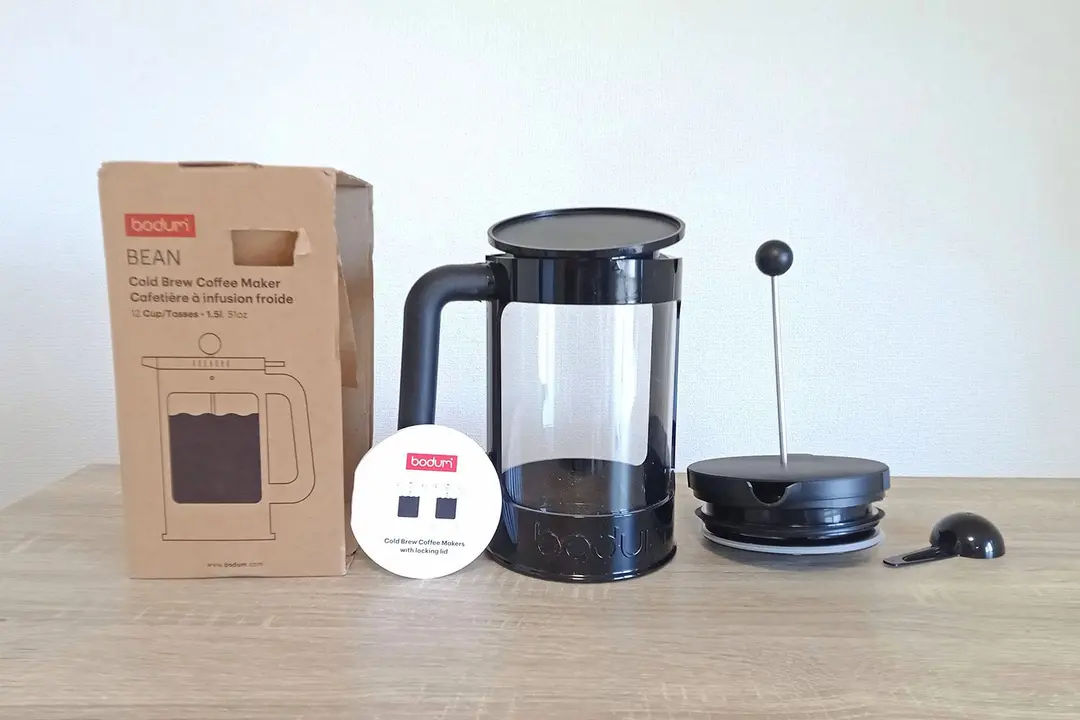 The unboxed Bodum cold brew coffee maker. To the right of the box  is the brew carafe, plunge filter lid, and then a spoon.