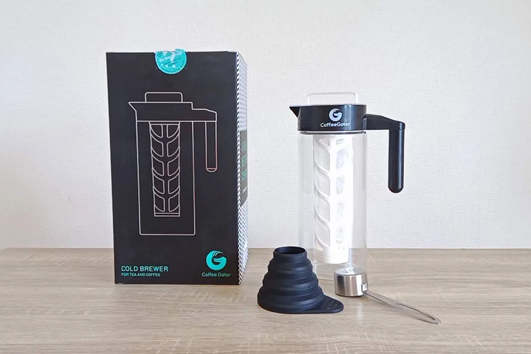 An unboxed Coffee Gator cold brew coffee maker. The box is to the left, a measuring spoon and silicone funnel are upfront.