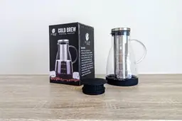 The Bean Envy cold brew coffee maker pictured alongside its box and its unique additional decanting lid.