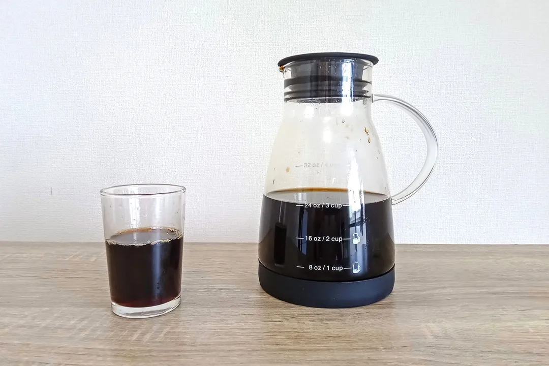 A glass of cold-brewed coffee standing in front of a carafe with a freshly brewed batch of coffee