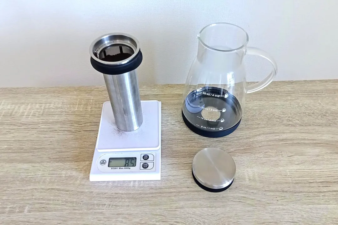 The stainless steel filter on a scale filled with coffee grounds standing next to a glass brew carafe.
