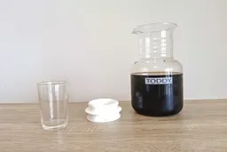 The Toddy System carafe filled with fresh cold-brewed coffee. The carafe is pictured next to the carafe stopper and a glass.