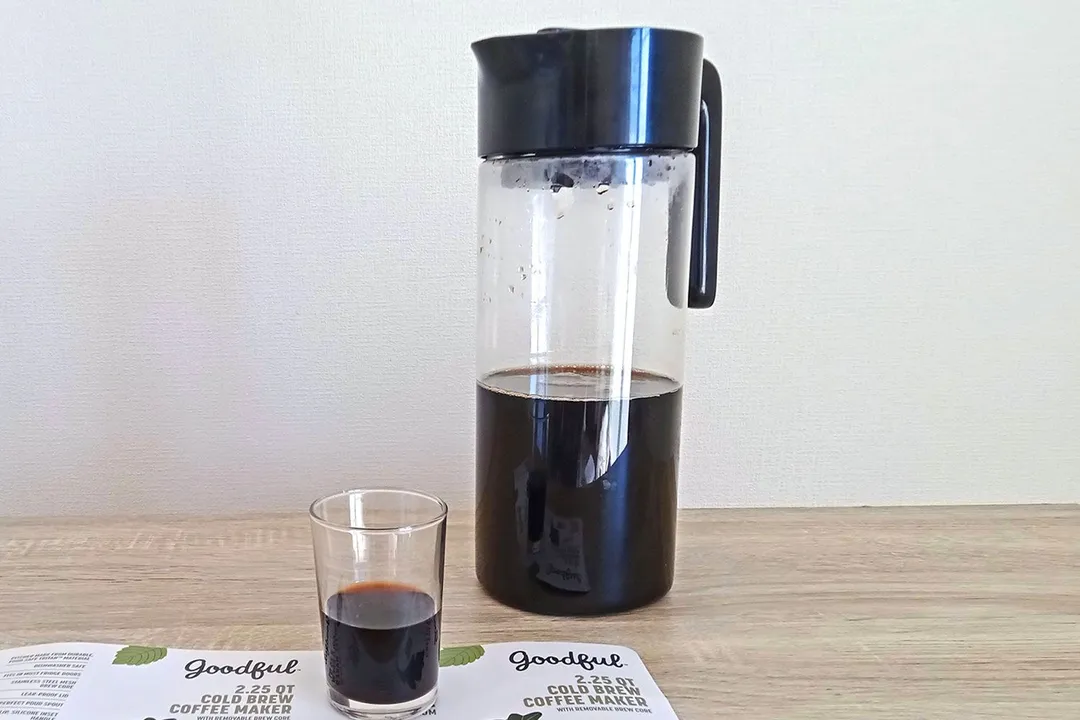 A glass of coffee resting on the product leaflet with the Goodful cold brew coffee maker behind.