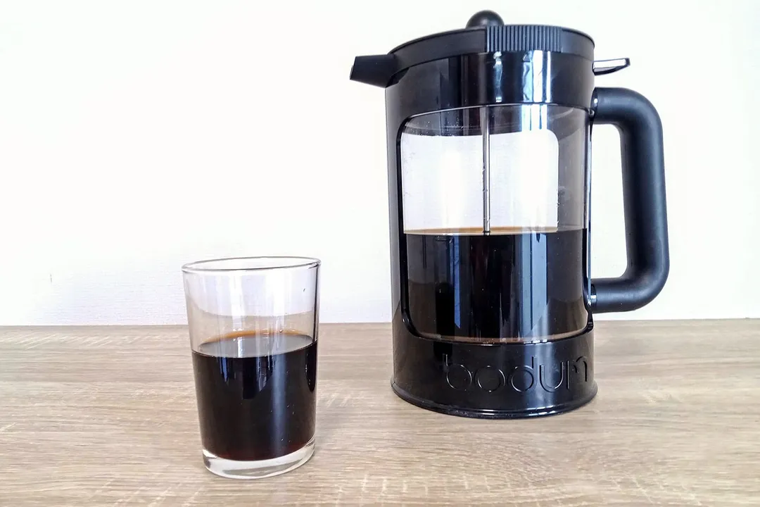 A glass of cold-brewed coffee standing near a brew carafe half-filled with coffee.