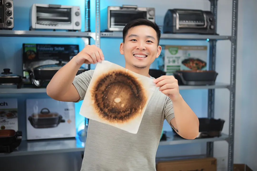 A person in a gray shirt holding an oil absorbent sheet with dark caramelized circles.