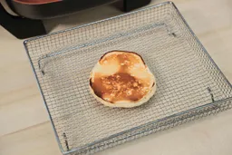 The bottom side of a golden brown pancake that’s dark around the edges inside an air fryer basket. In the corner is the Bella Non-Stick Electric Skillet 14607.