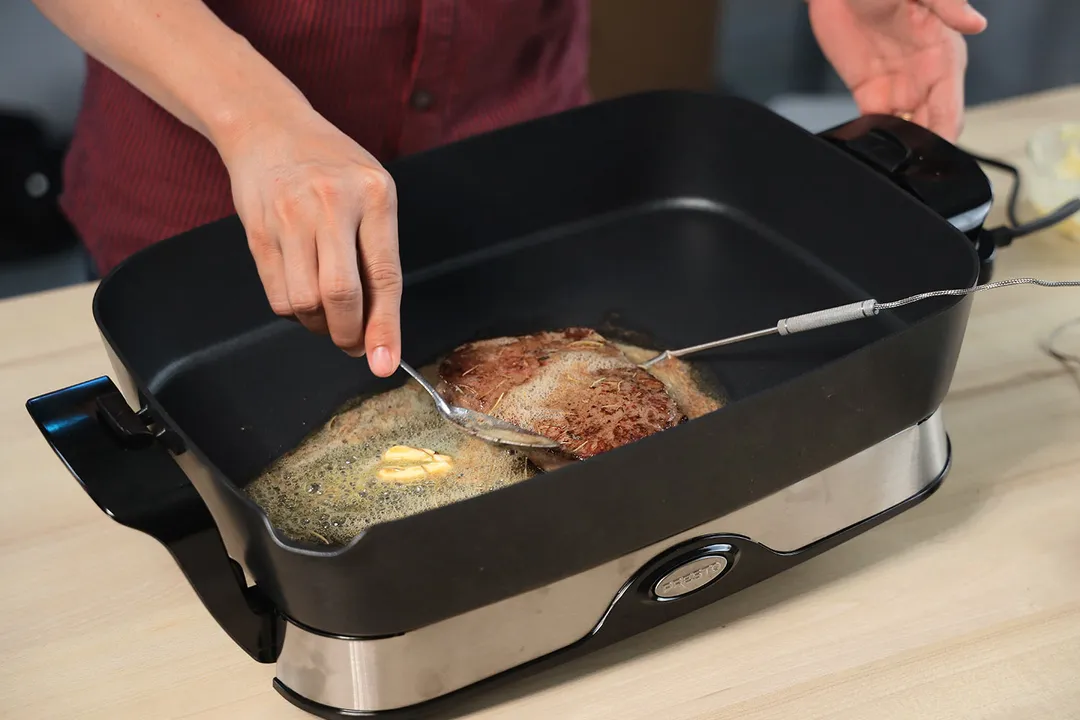 Coating a steak with butter inside the Presto Foldaway Non-Stick Electric Skillet 06857.